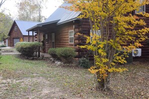 A rustic log cabin with a metal roof, surrounded by a yard with a small tree and bushes. - Marfly Mount Olive Retreat (Melbourne)