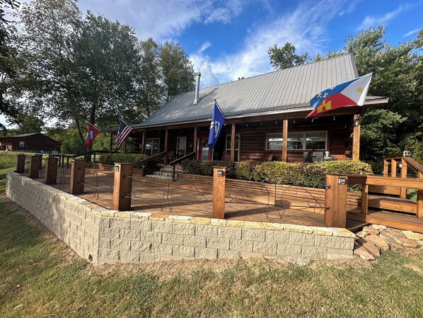 A rustic lodge with a stone retaining wall, wooden deck, and a flagpole with multiple flags. - Marfly Mount Olive Retreat (Melbourne)