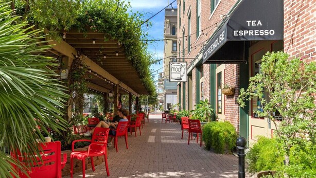 An outdoor cafe with red chairs and tables, a covered seating area, and a building with a 'Tea Espresso' sign. - Chic Historic Loft, 3 Blocks from The Strand (Galveston)