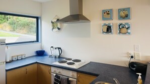 A modern kitchen with a stove, kettle, and a window overlooking greenery. - Peaceful piece of Paradise (Wainui)