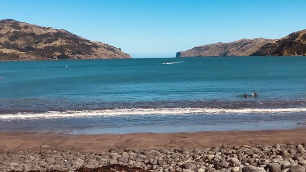 A beach with rocky shoreline, calm sea, and hills in the background. - Peaceful piece of Paradise (Wainui)
