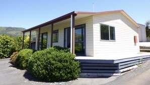 A single-story mobile home with a covered porch, large windows, and a flat roof. - Peaceful piece of Paradise (Wainui)