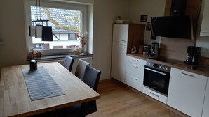 A modern kitchen with a wooden table and chairs, a refrigerator, a stove, and a window with a view of the outside. - Very nice apartment with garden, perfect starting point for hikes, bike tours etc.   (Hürtgenwald)