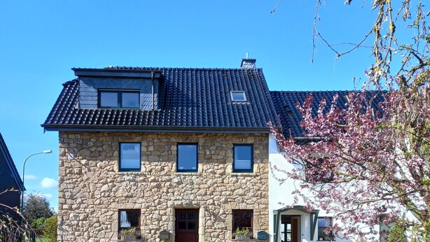 A stone house with a tiled roof, a front porch, and a small garden area. - Very nice apartment with garden, perfect starting point for hikes, bike tours etc.   (Hürtgenwald)