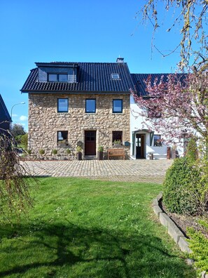 Une maison en pierre avec un toit en tuiles, un porche à l’avant et un petit jardin.