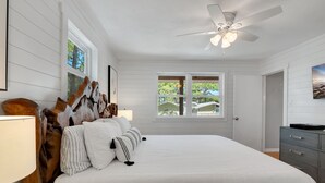 Ein Schlafzimmer mit einem großen Bett, einem Deckenventilator, einem Fenster mit Blick auf Häuser und einem Schminktisch.