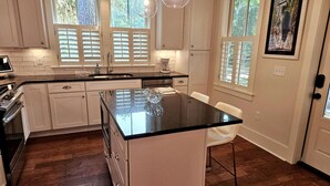 A kitchen with white cabinets, a black countertop, and a large island. There are two pendant lights above the island. - Low Country Cottage in Beautiful Habersham (Beaufort)