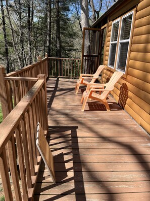 Une terrasse en bois avec deux chaises Adirondack et une rambarde en bois.