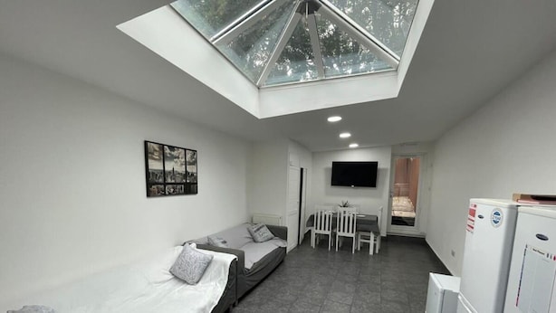 A compact room with a skylight, a bed, a small table with chairs, a TV, and a refrigerator. - Studio Close to Selly Oak Train Station (Birmingham)