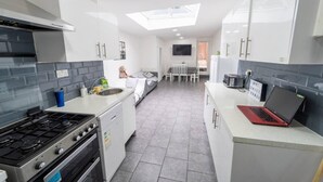 A modern kitchen with a gas stove, oven, and a microwave. There is a dining area with a table and chairs, and a TV mounted on the wall. - Cosy Studio Close to the University (Birmingham)