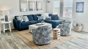 Een moderne woonkamer met een donkerblauwe modulaire bank, gestreepte poufs, een klein houten bijzettafeltje en een witte vloerkleed.