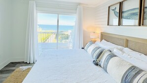Een slaapkamer met een groot bed, uitzicht op de oceaan en een plafondventilator.
