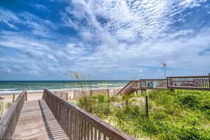 A wooden boardwalk leading to a beach with a view of the ocean and a clear sky.