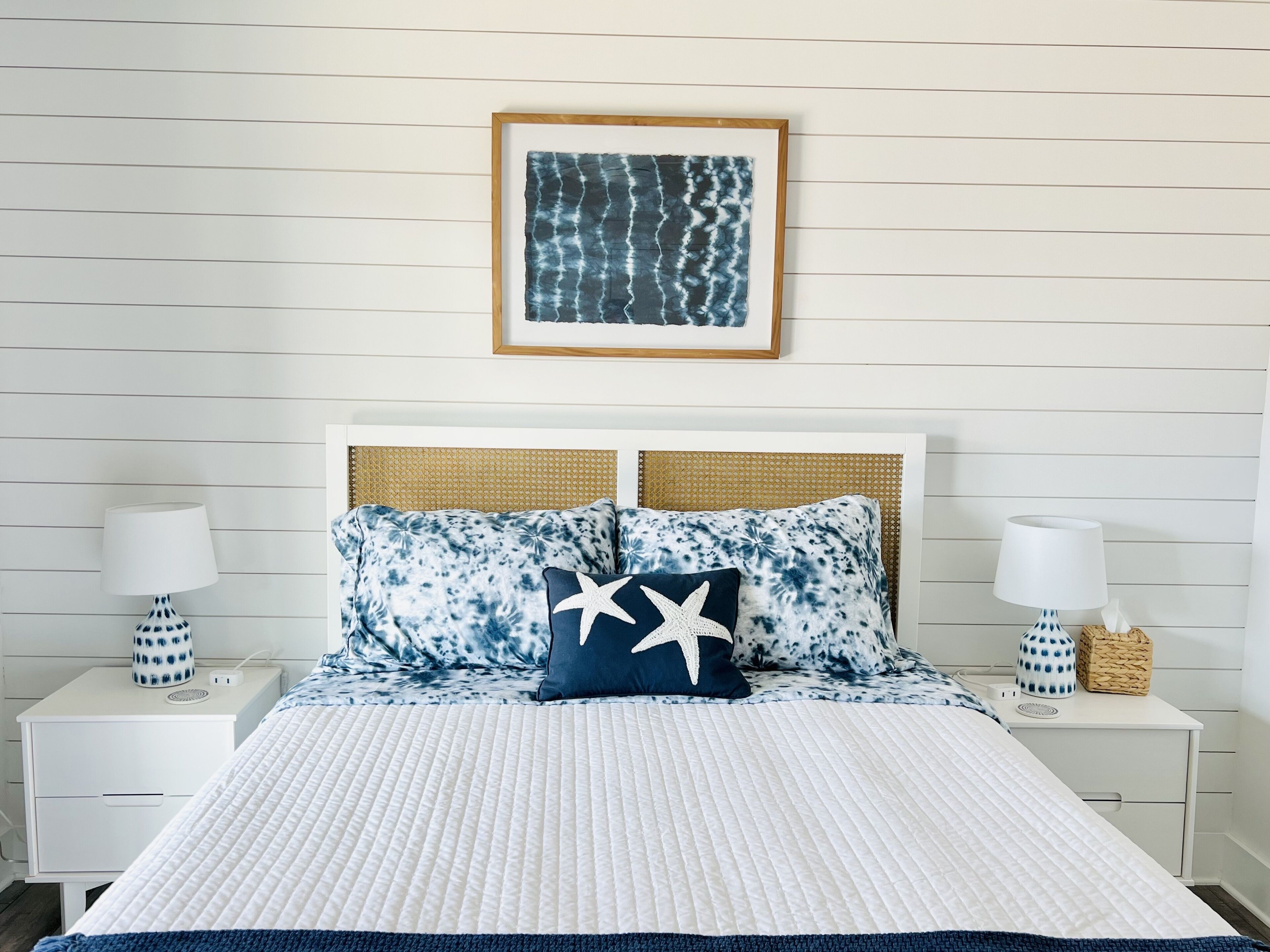 A neatly arranged bedroom with a white bedspread, two matching pillows with a star design, and a framed artwork above the bed.