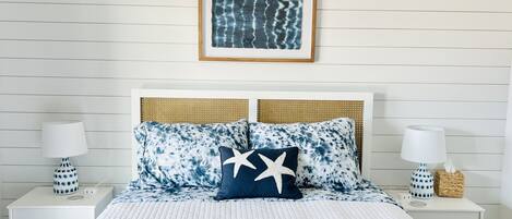 A neatly arranged bedroom with a white bedspread, two matching pillows with a star design, and a framed artwork above the bed.