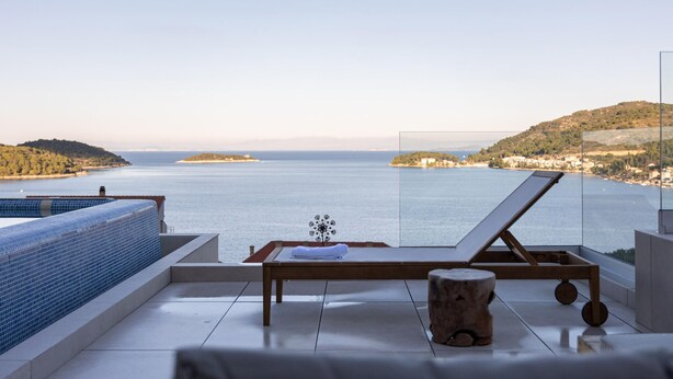 Eine sonnendurchflutete Terrasse mit Meerblick, ein Liegestuhl, ein kleiner Tisch und ein dekorativer Gegenstand.