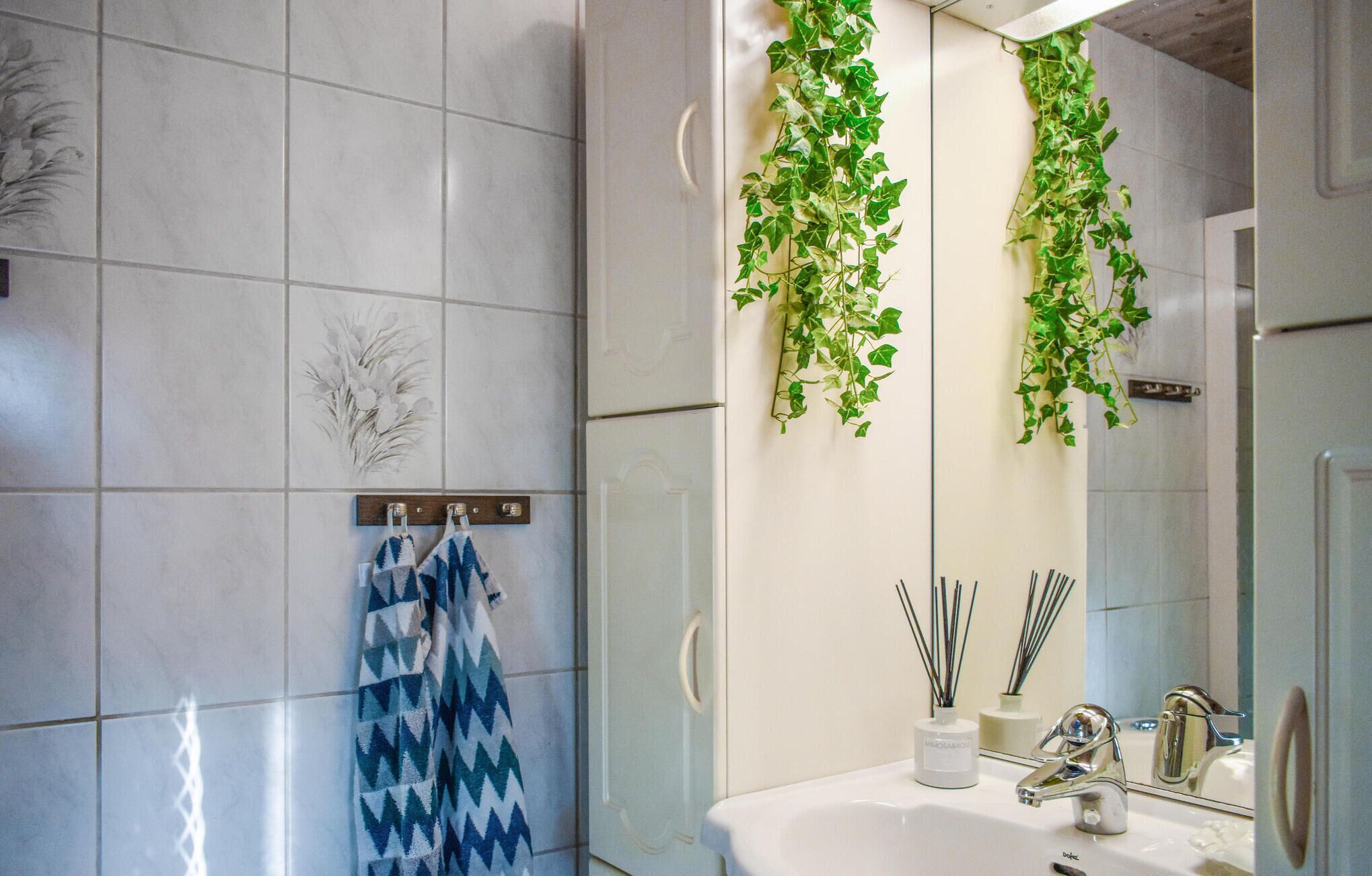 Ein Badezimmer mit einem weißen Waschbecken, einem Spiegel und hängenden Pflanzen an der Wand.