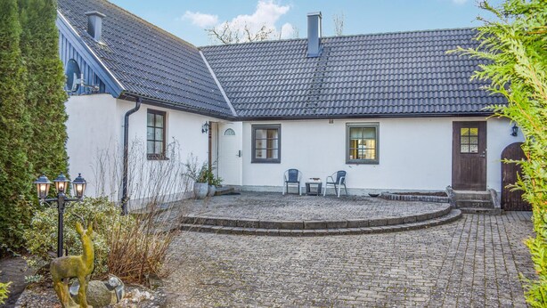 A white house with a tiled roof, a stone courtyard, and a small garden area with a statue.