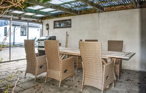 A covered outdoor patio with a table and wicker chairs, a grill, and a view of a building in the background. - Amazing home in Klagstorp with WiFi (Klagstorp)