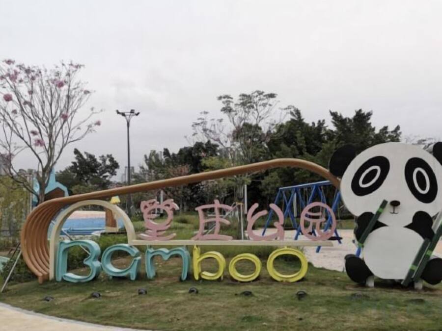 Une aire de jeux avec une grande sculpture de panda, des balançoires et un toboggan.