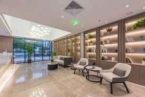 A modern lobby with a glass wall, seating area, and bookshelves. - Wei Hotel Fan (Beijing Wangjing SOHO Yitong Subway Station) (Beijing)