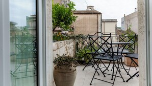 Une petite terrasse extérieure avec une table et des chaises, entourée de plantes en pot et d’un mur de pierre.
