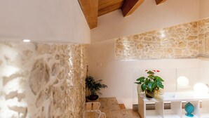 Une cuisine moderne avec des murs en pierre, des poutres en bois et un plan de travail blanc agrémenté d’une plante en pot.