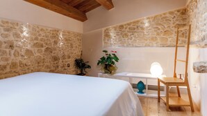 Une chambre avec des murs en pierre, un plafond en bois, un lit, un bureau, une chaise et une lampe.