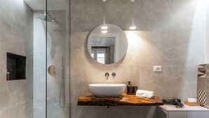 Une salle de bain moderne avec un grand lavabo ovale, un miroir rond et un espace douche.