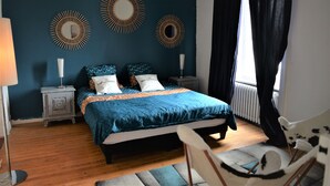Un dormitorio con cama, dos mesitas de noche, una silla y espejos decorativos en la pared.