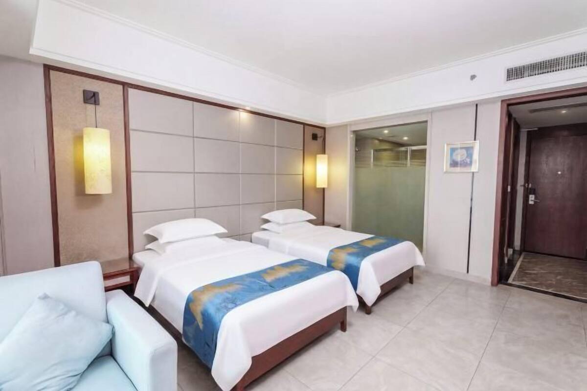 A hotel room with two beds, a seating area, and a door leading to a hallway.