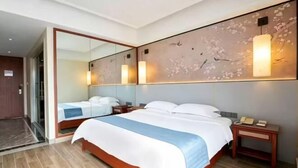 A hotel room with a large bed, a nightstand, a mirror, and a wall-mounted light fixture. - Yihao Hotel (Qionghai)