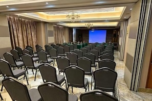 Ein Konferenzraum mit Reihen von Stühlen, einer Bühne mit blauem Hintergrund und einer Kristallleuchtre.