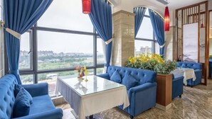 A room with a large window, blue upholstered sofas, a glass coffee table, and a red hanging light fixture. - Yihao Hotel (Qionghai)