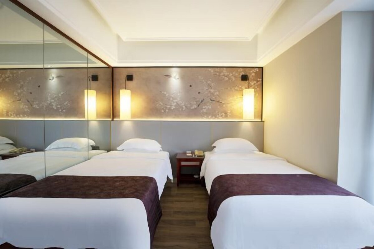 A hotel room with two beds, a large mirror, and a wall-mounted light fixture.
