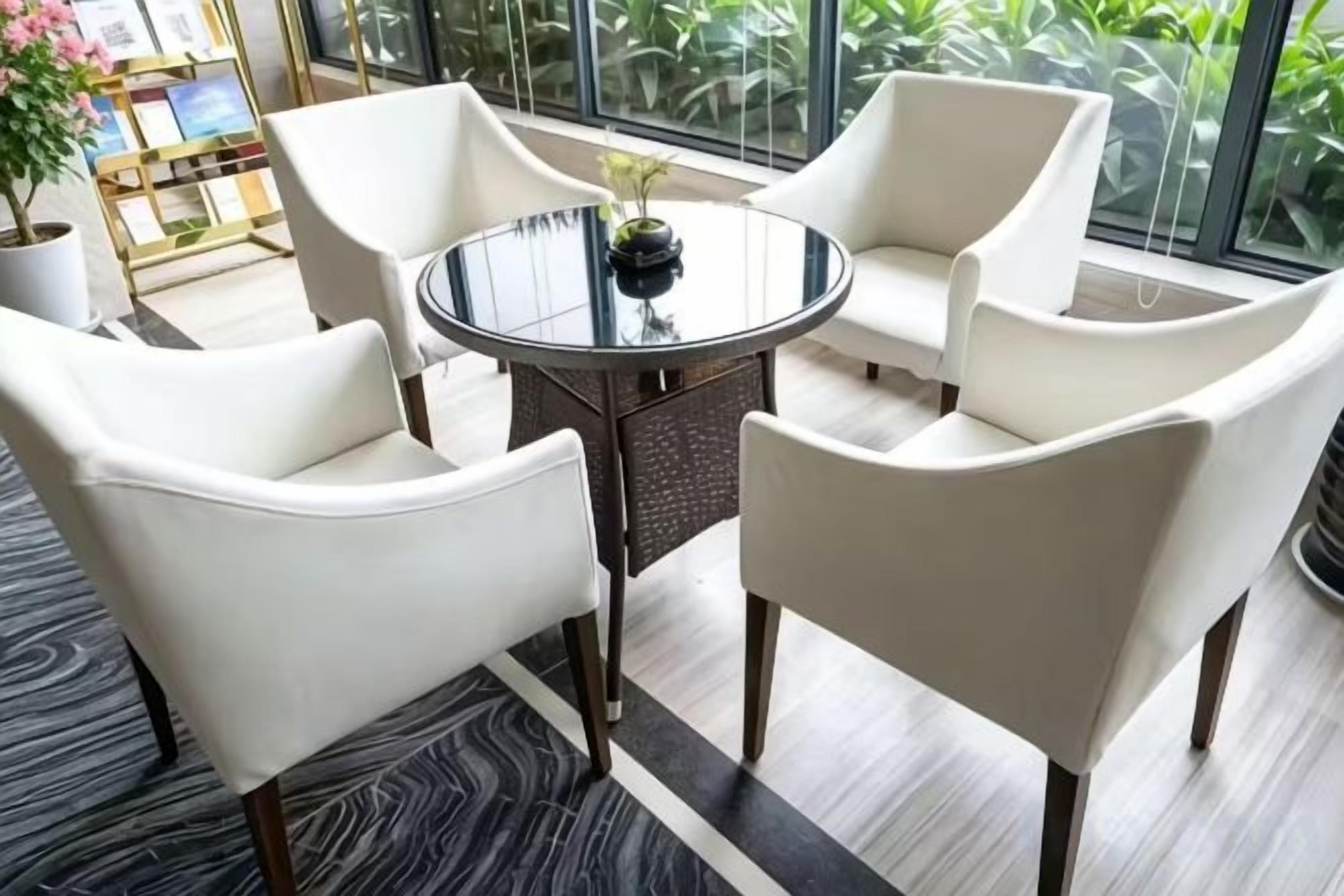 A modern room with a round glass table surrounded by four white chairs, a potted plant, and a bookshelf with books and decorative items.
