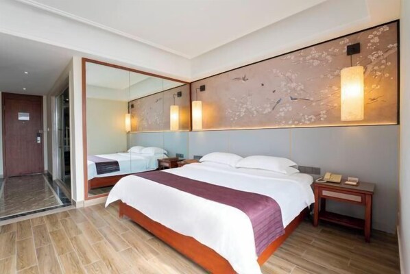 A hotel room with a large bed, a nightstand with a phone, a mirror, and a wall-mounted light fixture. - Yihao Hotel (Qionghai)