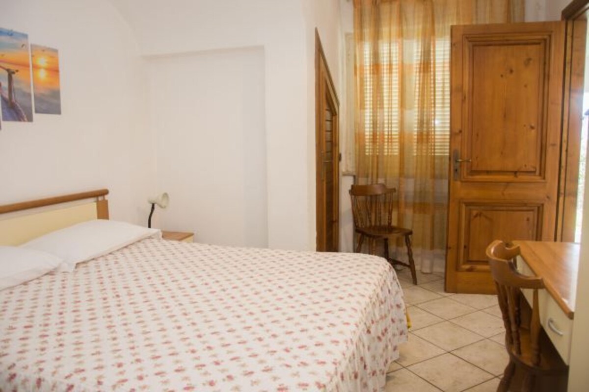 Un dormitorio con cama, una silla, una puerta de madera y una ventana con cortinas.