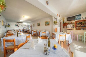 A restaurant with multiple tables and chairs, a bar area with bottles, and a television on the wall. - Villa Mena (Forio)