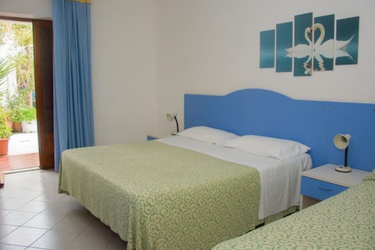 Habitación de hotel con cama, mesita de noche, lámpara y una obra de arte en la pared.