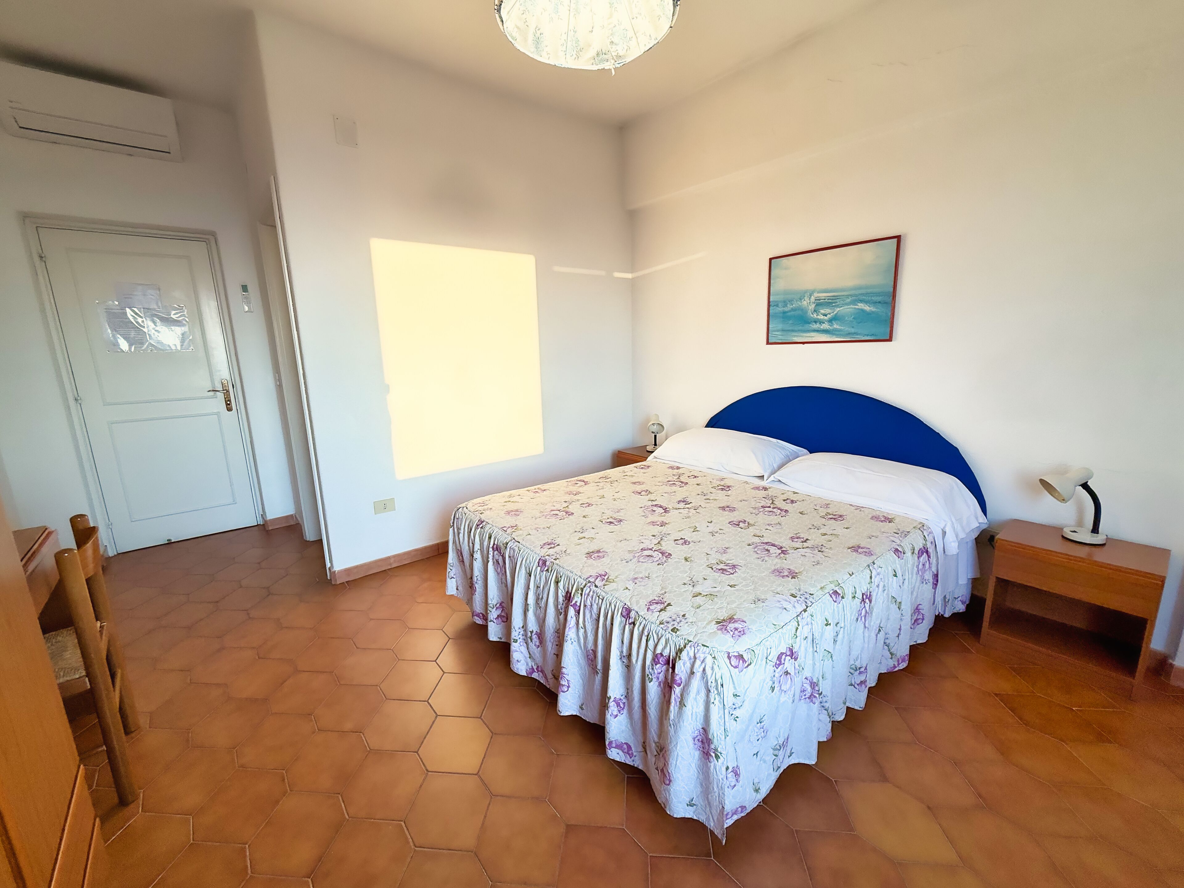 A bedroom with a bed, a nightstand, a lamp, a painting, and a door.