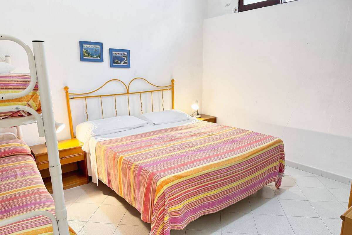 Una cama individual con una colcha a rayas de colores, una mesita de noche con una lámpara y dos cuadros en la pared.