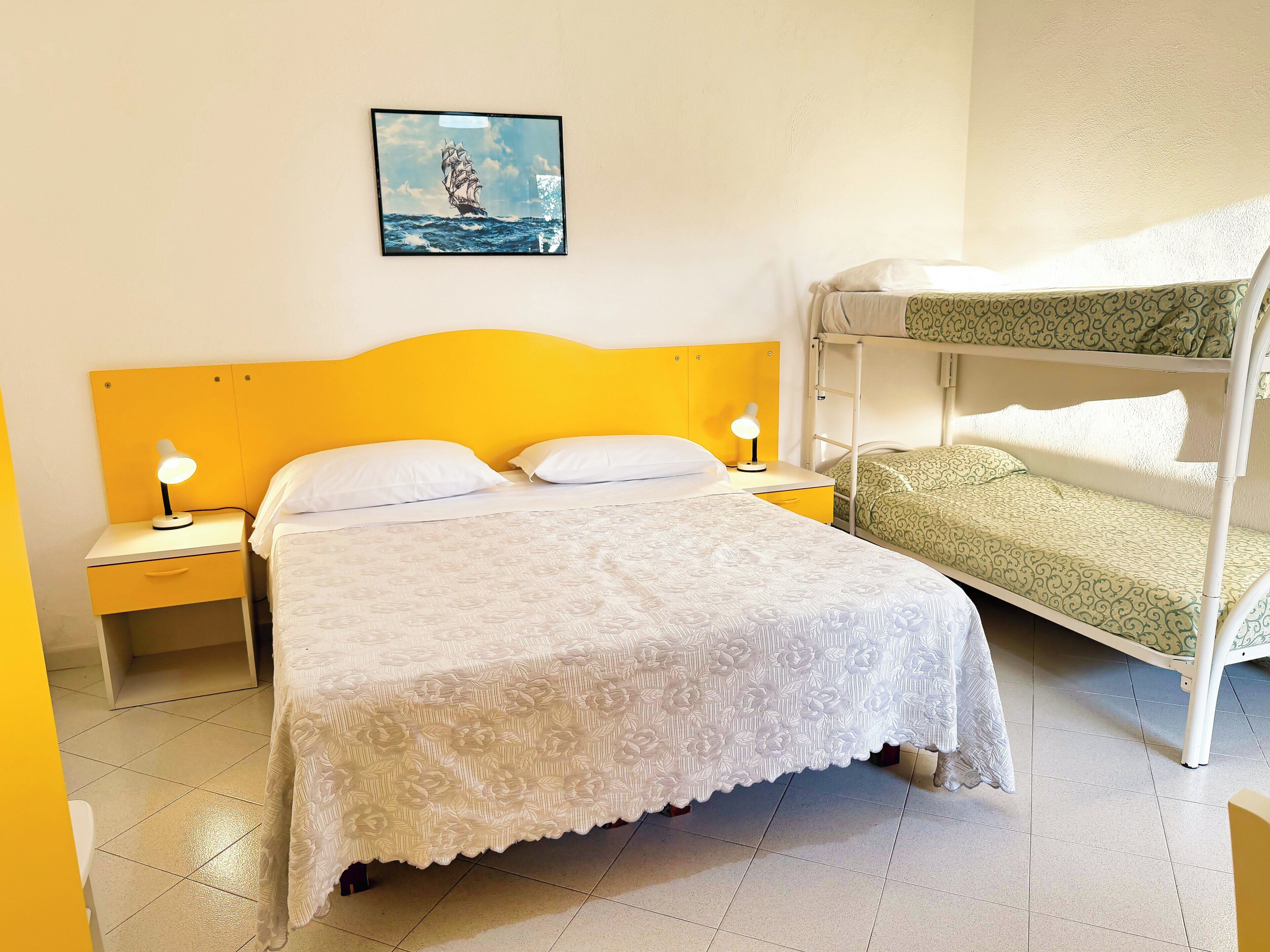 A room with a bed, a nightstand, a lamp, a bunk bed, and a painting on the wall.