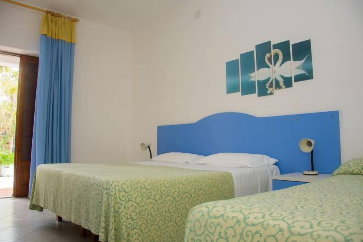 Una habitación con dos camas, un cabecero azul y un cuadro de un cisne en la pared.