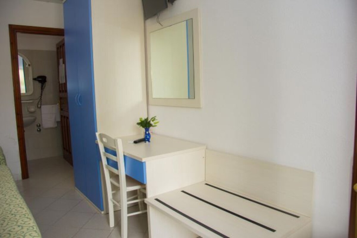 Una habitación pequeña y limpia con un escritorio blanco, una silla, un espejo y una planta pequeña.