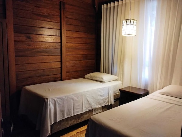 A single bed with a white mattress and pillow, a wooden headboard, a nightstand, and a hanging light fixture. - VIA SPE - Pousada (Belo Horizonte)