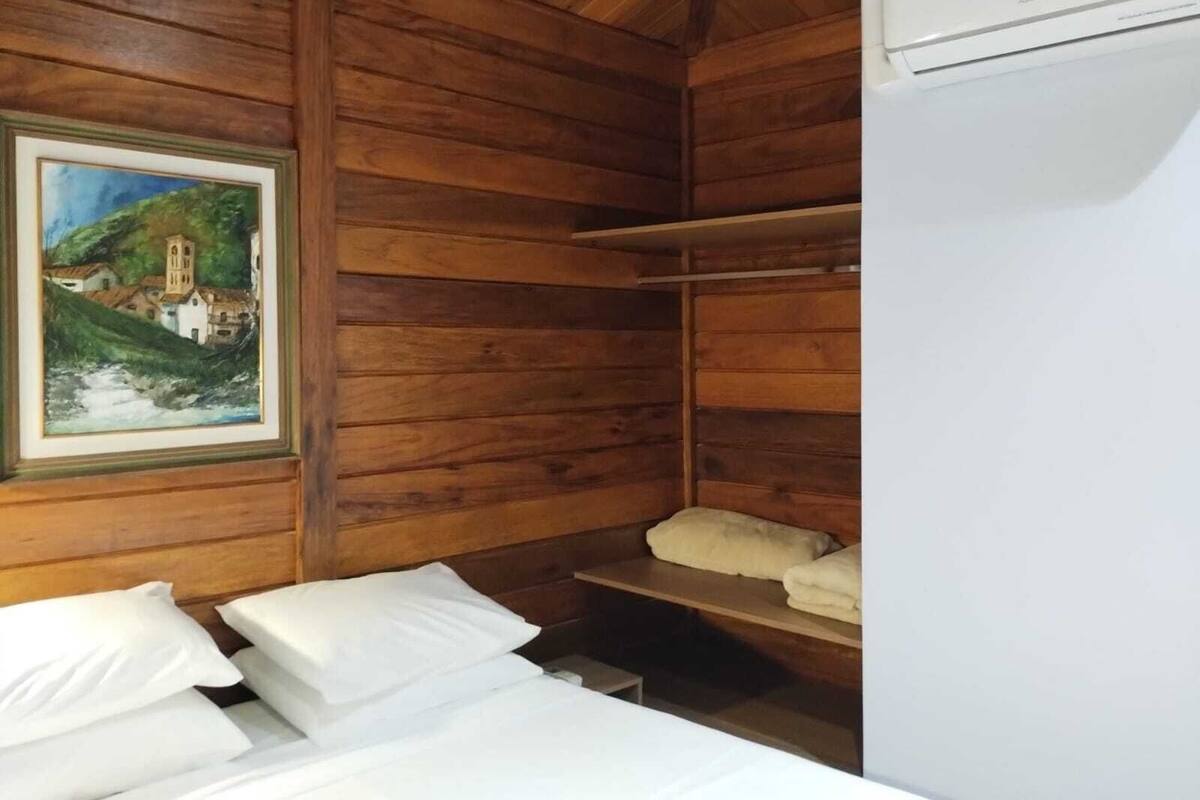 Une chambre rustique en bois, avec un lit, un tableau et une étagère où sont posées des serviettes.