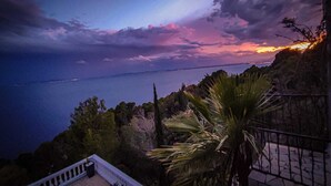 A coastal view with a sunset over the sea, a palm tree, and a balcony with a railing. - Maison Paradisiaque A Rosas A Proximite DES Plages (CANYELLES ALMADRABA (AJUNTAMENT ROSES))