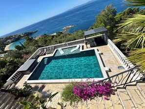 Una piscina amb vistes al mar, envoltada d'escales de pedra i vegetació.