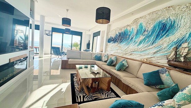 A modern living room with a large window, a sofa, a coffee table, and a decorative wall piece. - Maison Paradisiaque A Rosas A Proximite DES Plages (CANYELLES ALMADRABA (AJUNTAMENT ROSES))